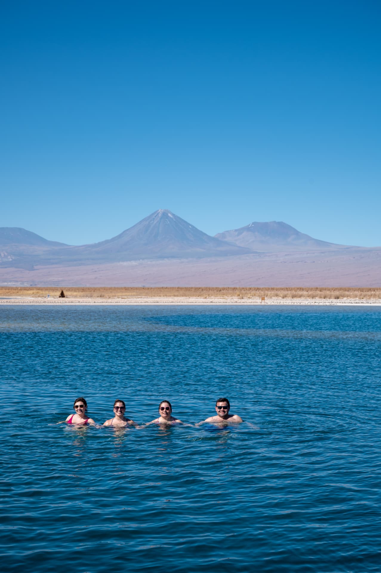 Equipe flutuando em laguna com vulcão Licancabur ao fundo