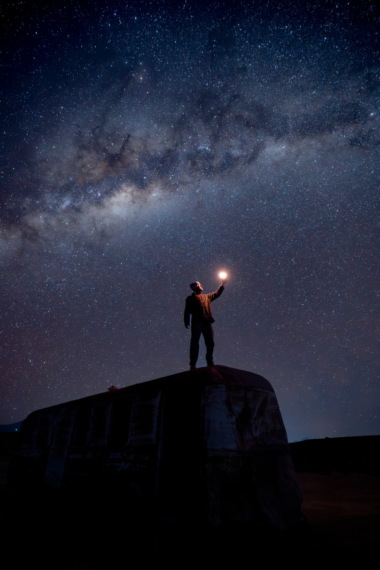 Viajante em pé sobre o bus da Grado 10 segurando uma luz sob a Via Láctea no Deserto do Atacama