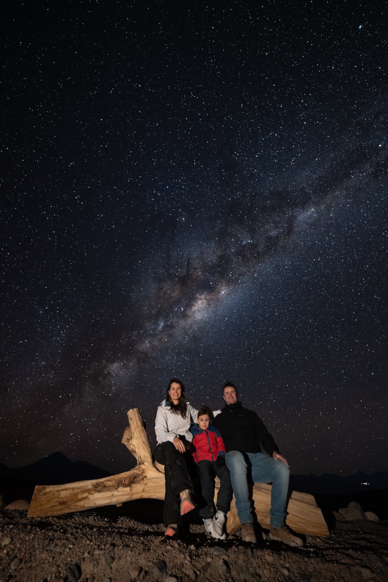 Família apoiada em tronco no deserto com o céu estrelado ao fundo
