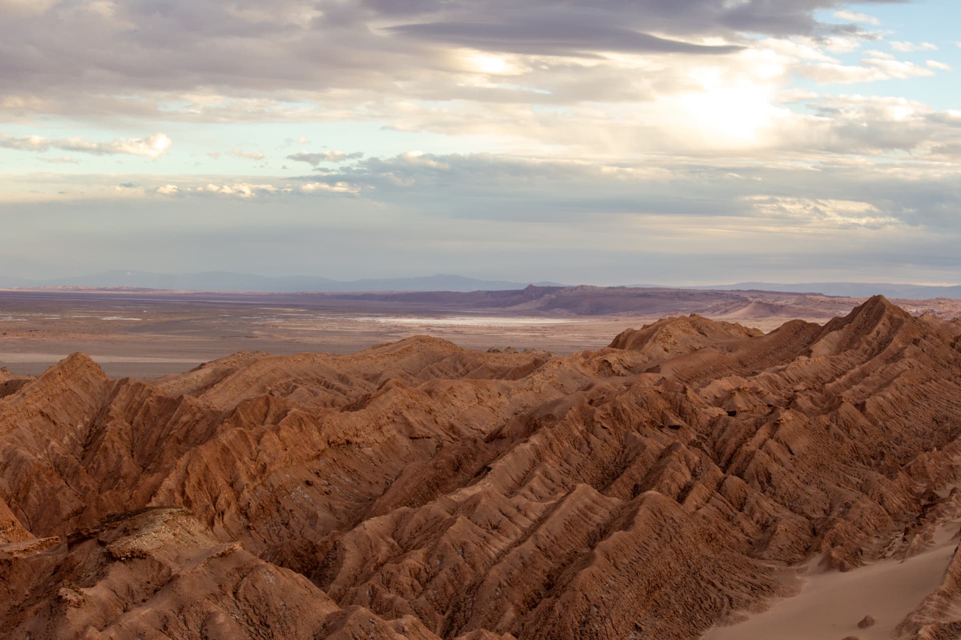 Panorama do Vale da Lua no Atacama ao entardecer, com formações rochosas onduladas e planícies ao fundo