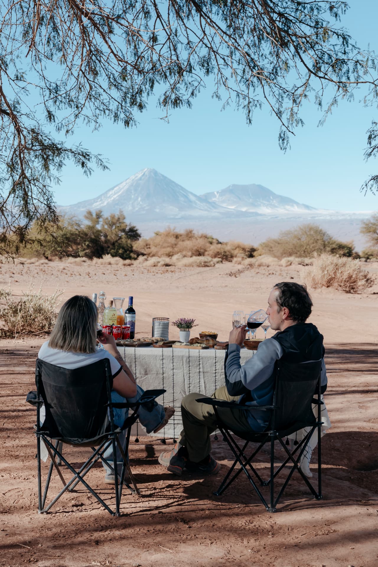 Casal desfrutando um momento gastronômico ao ar livre no Deserto do Atacama, com vulcões ao fundo