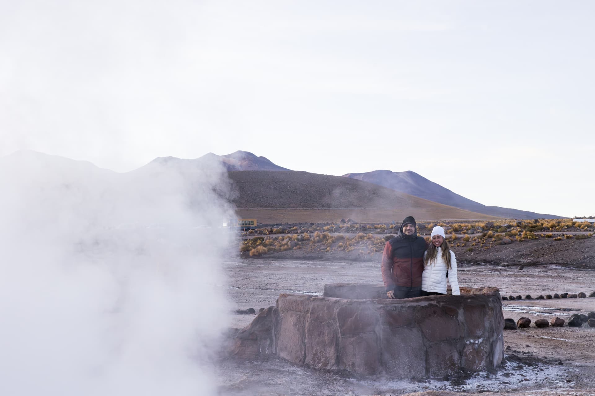 Casal sorrindo junto a uma fumarola nos Gêiseres del Tatio