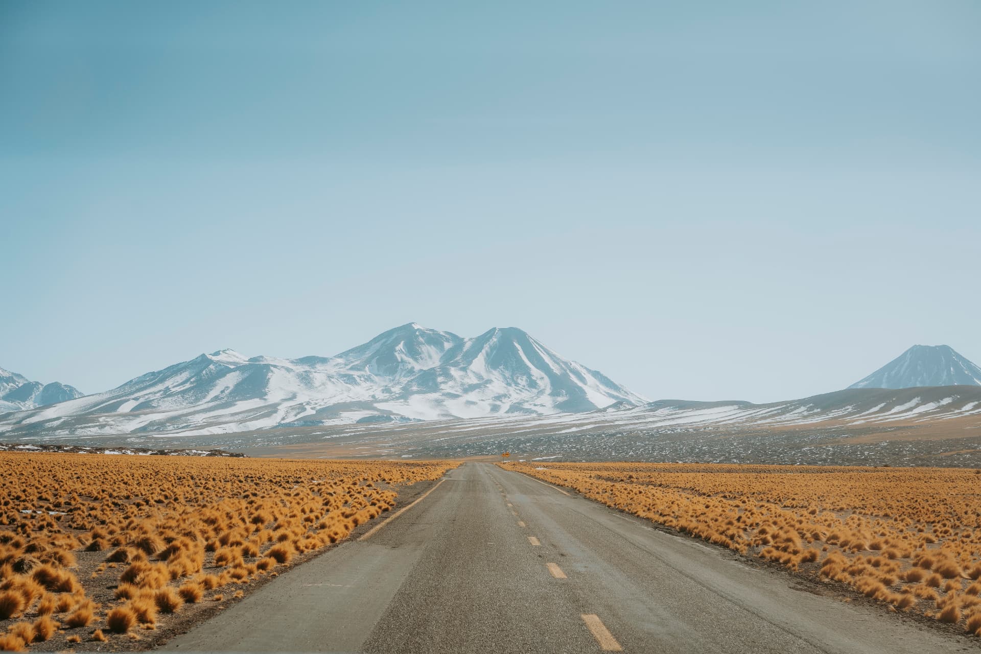 Estrada do Atacama com vulcões nevados ao fundo sob céu claro