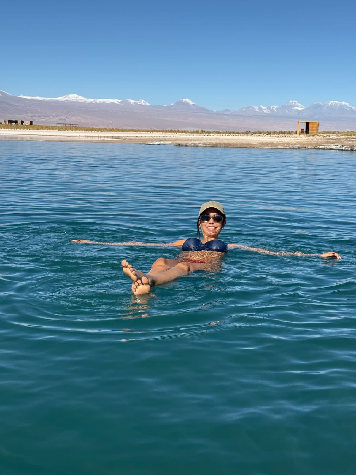 Viajante flutuando nas águas cristalinas da Laguna Cejar com montanhas ao fundo no Atacama