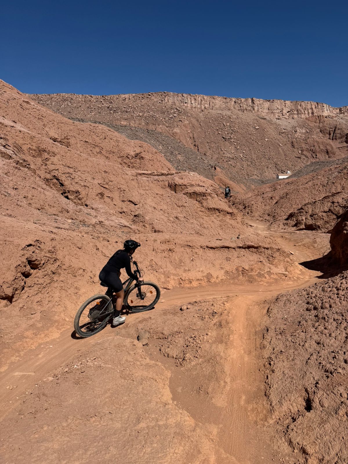 Ciclista pedalando pelo Vale de Catarpe entre formações rochosas avermelhadas no Atacama