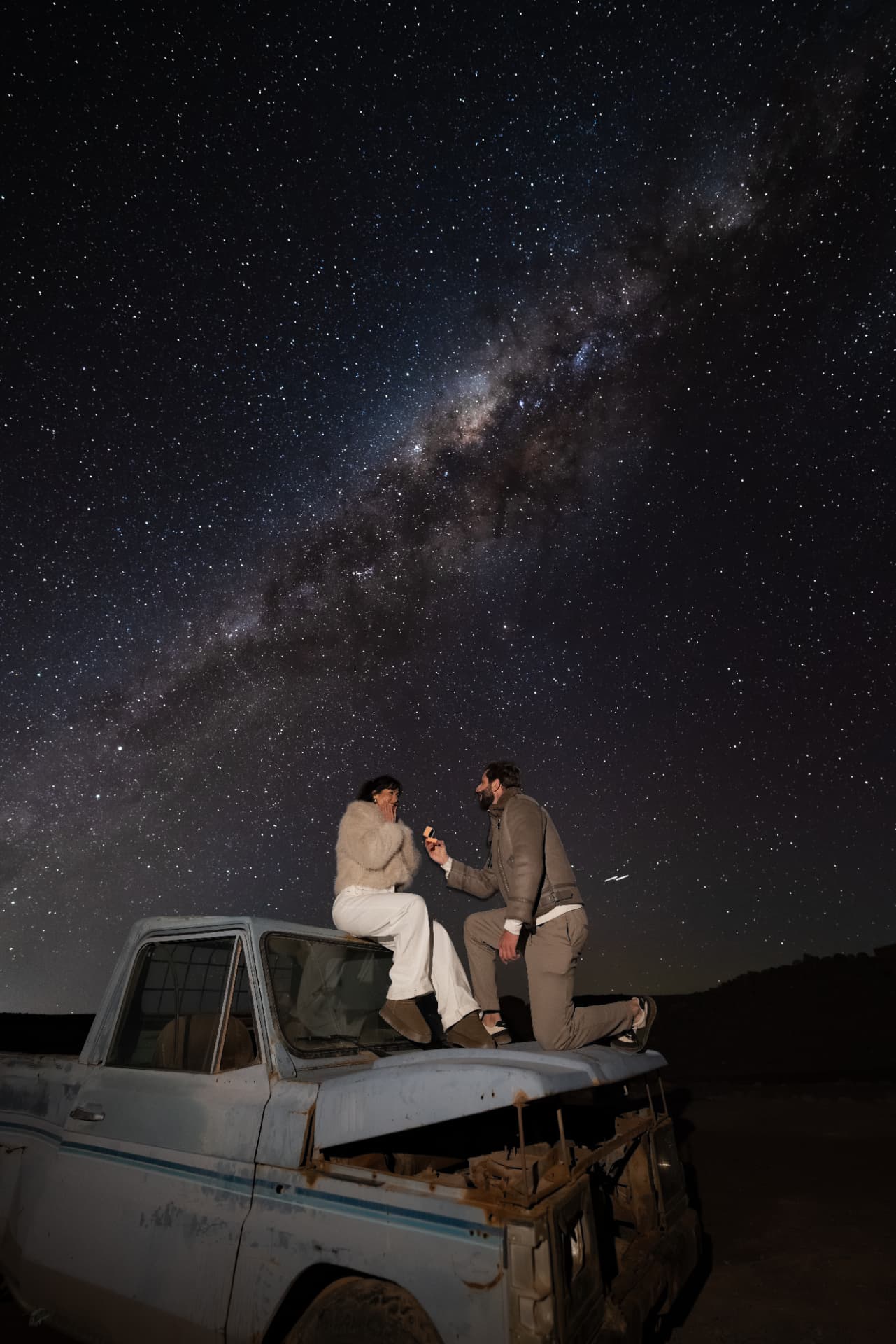 Casal com anel de noivado sobre um caminhão antigo sob a Via Láctea durante o Tour Astronômico - Orbit 10 no Atacama