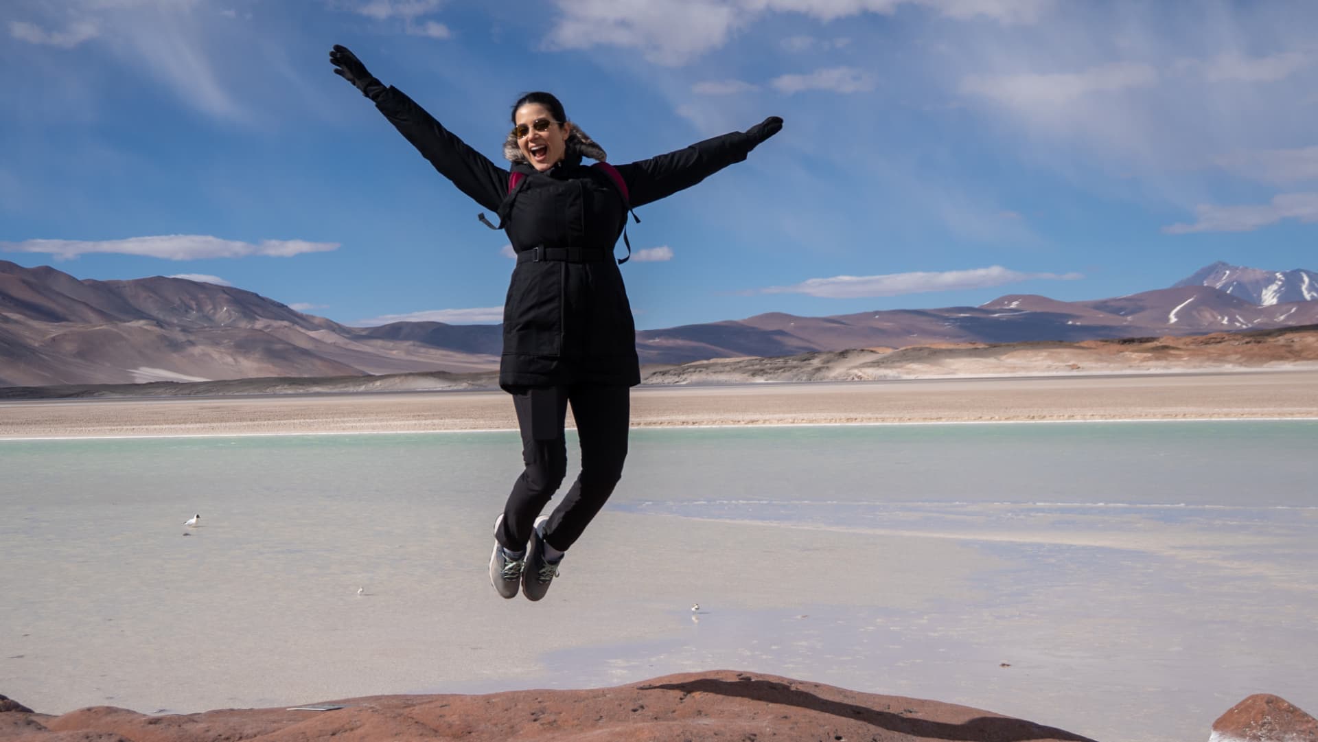 Viajante comemora com os braços abertos diante das lagoas altiplânicas e das montanhas do Atacama